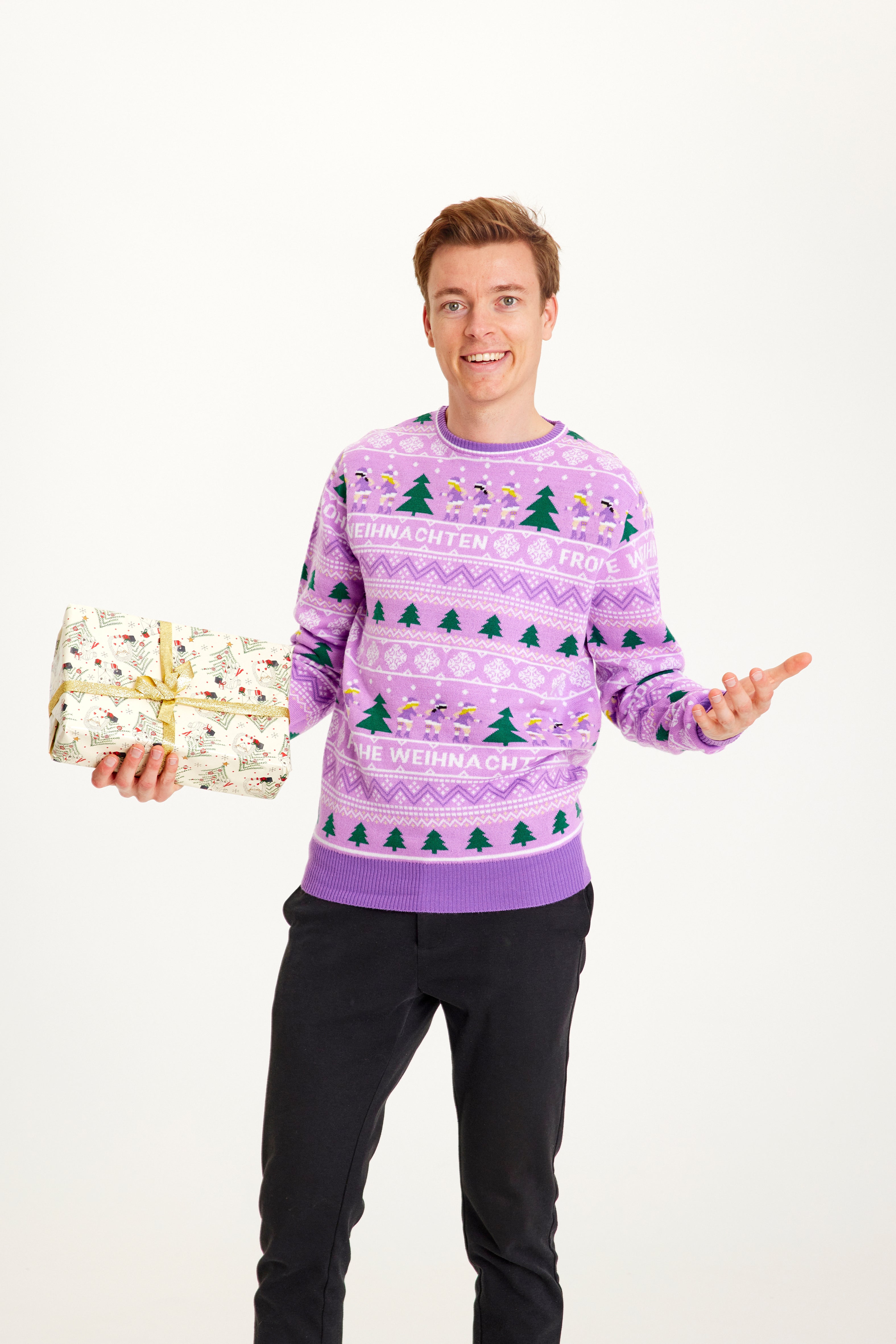 Een man met een cadeau in een paarse kersttrui met kerstbomen erop.